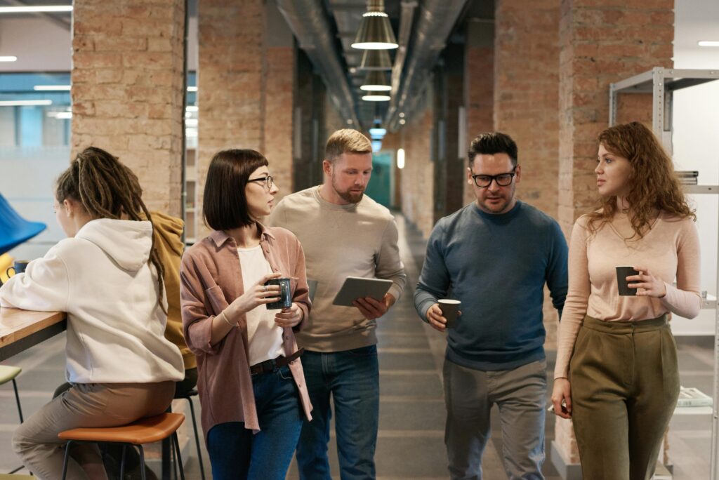 A diverse group of colleagues discussing a project in a modern office hallway.